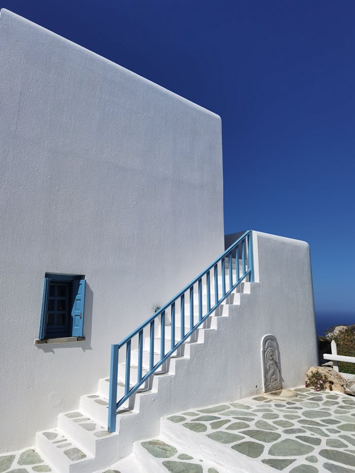 Minimalist Greek building with blue accents under clear skies, showcasing island charm.